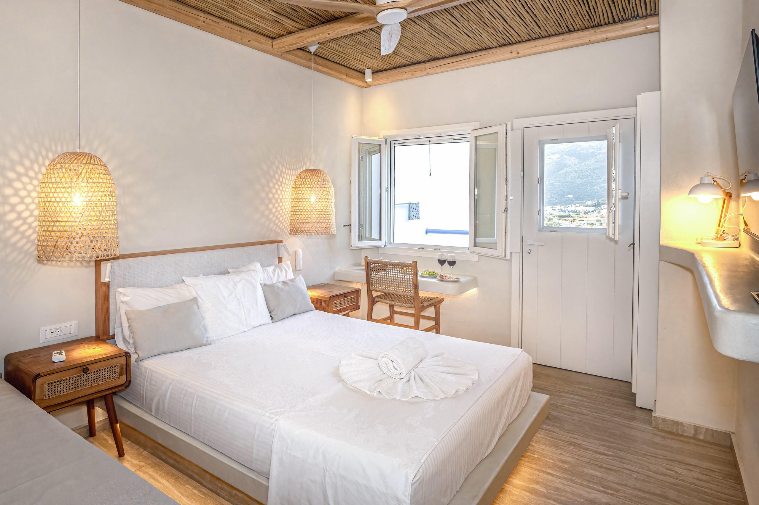 A renovated room with a bamboo ceiling, wicker lamp and white linen, its balcony door open to the bay
